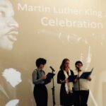 Three people on stage before microphones with a backdrop of Martin Luther King, Jr.