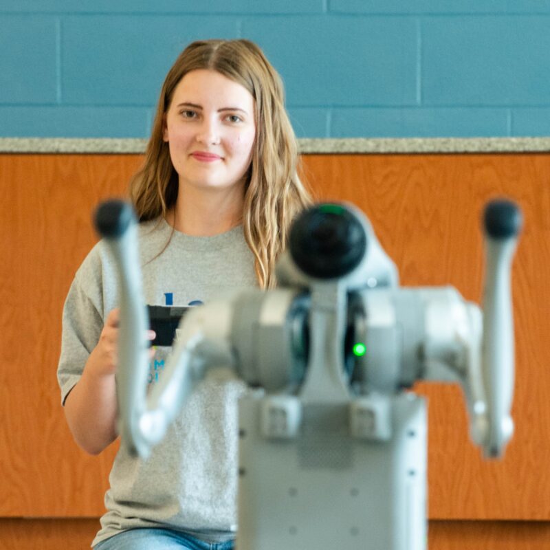 Student watches a robotic arm with a green light during a robotics and drones demonstration.
