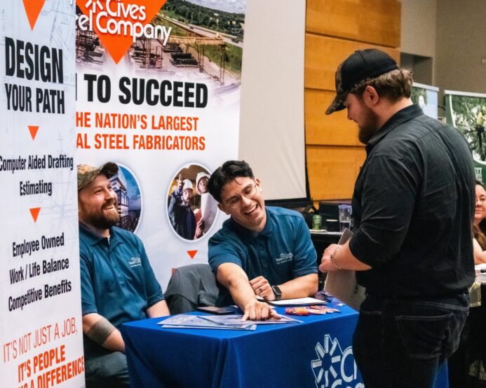 Three men talking at a career fair booth.