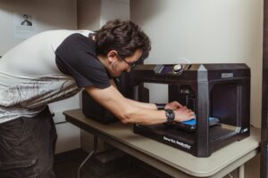 A student adjusting a 3D print on a MakerBot Replicator in a classroom lab.