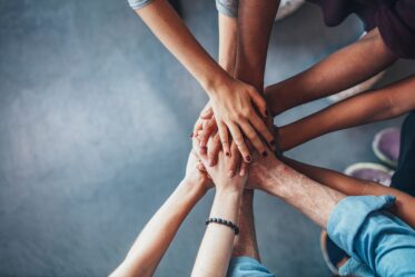 A photo of a close up top view of young people of all races putting their hands together.