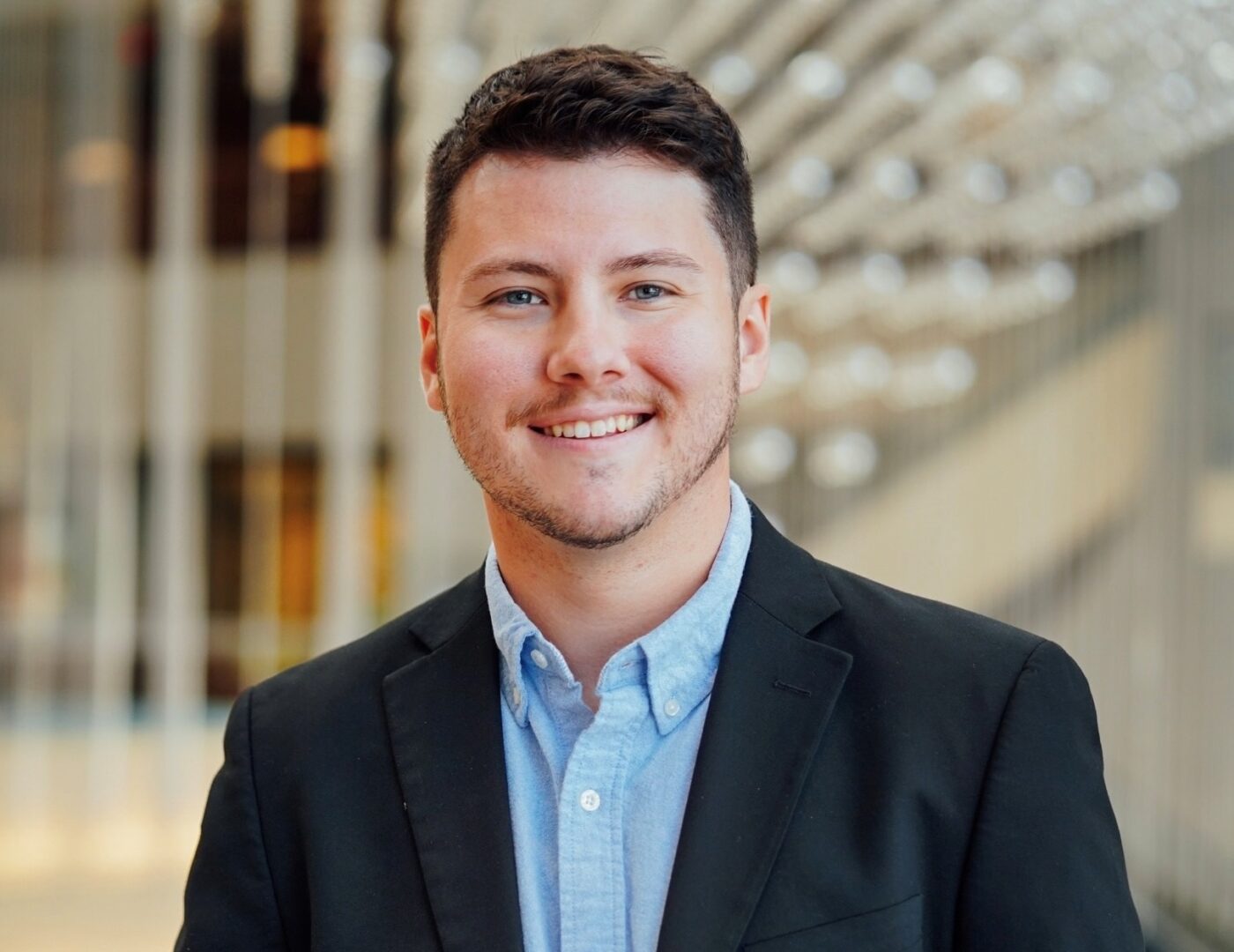 a man faces the camera and smiles wearing a dress shirt and blazer jacket