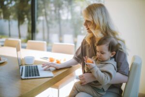 A mom uses a computer with a baby on her lap in a living room area