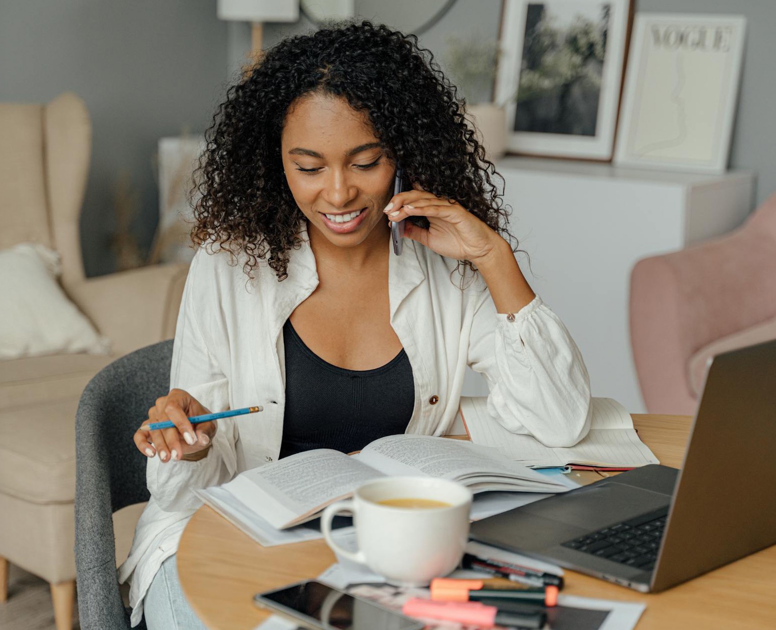 a photograph of an african american woman using a laptop and talking on the phone while at home