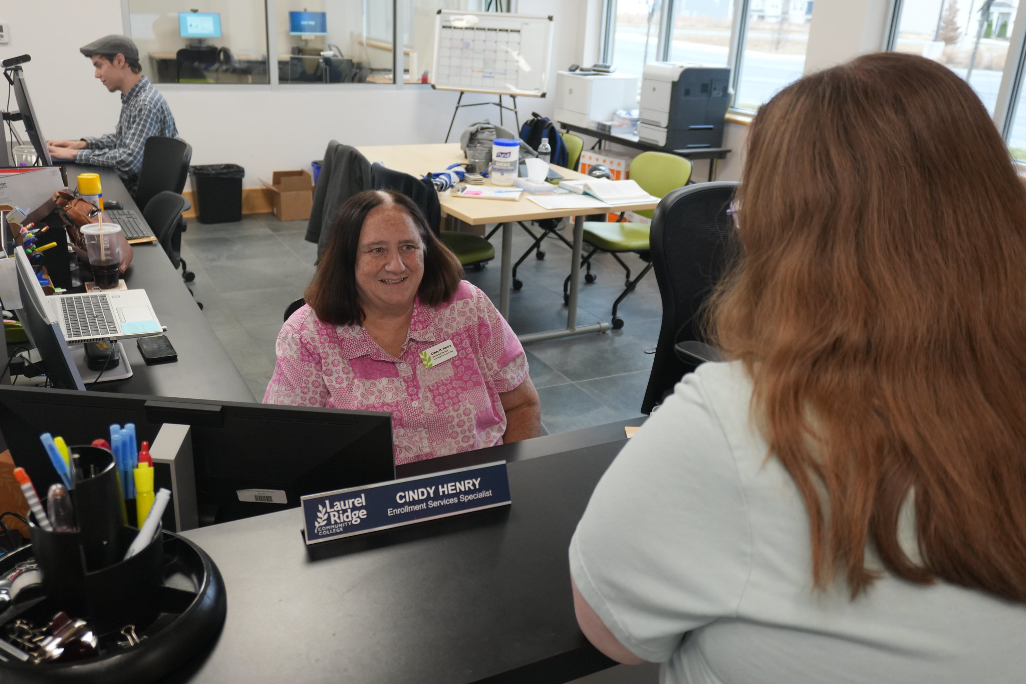 photo of a smiling Cindy Henry sitting behind a desk and greeting a person