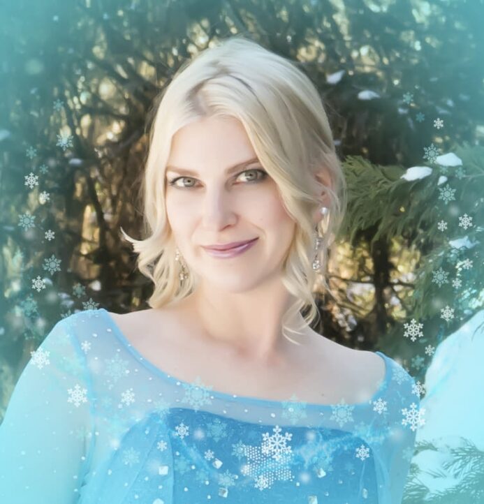 Breeden in a light blue dress standing outdoors among evergreen trees, with a soft winter-themed snowflake overlay.