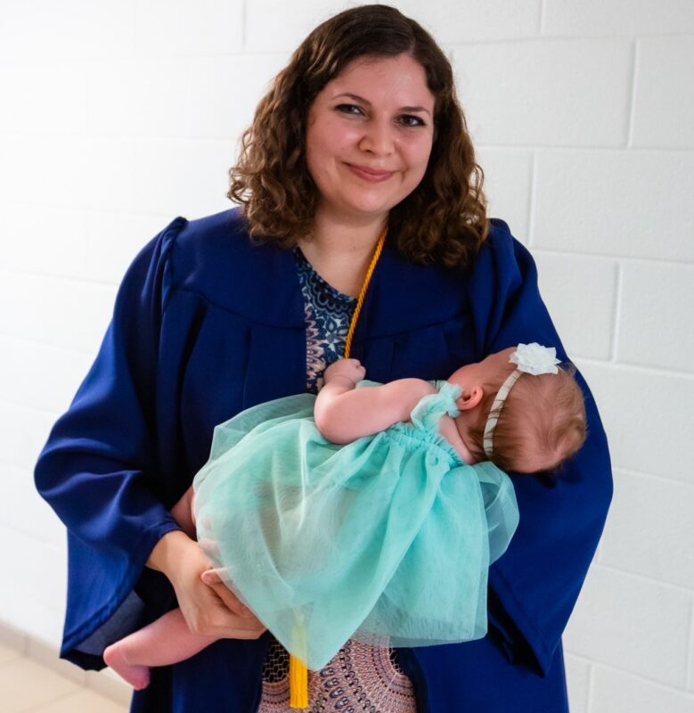 a graduate wearing a graduation gown and holding an infant baby