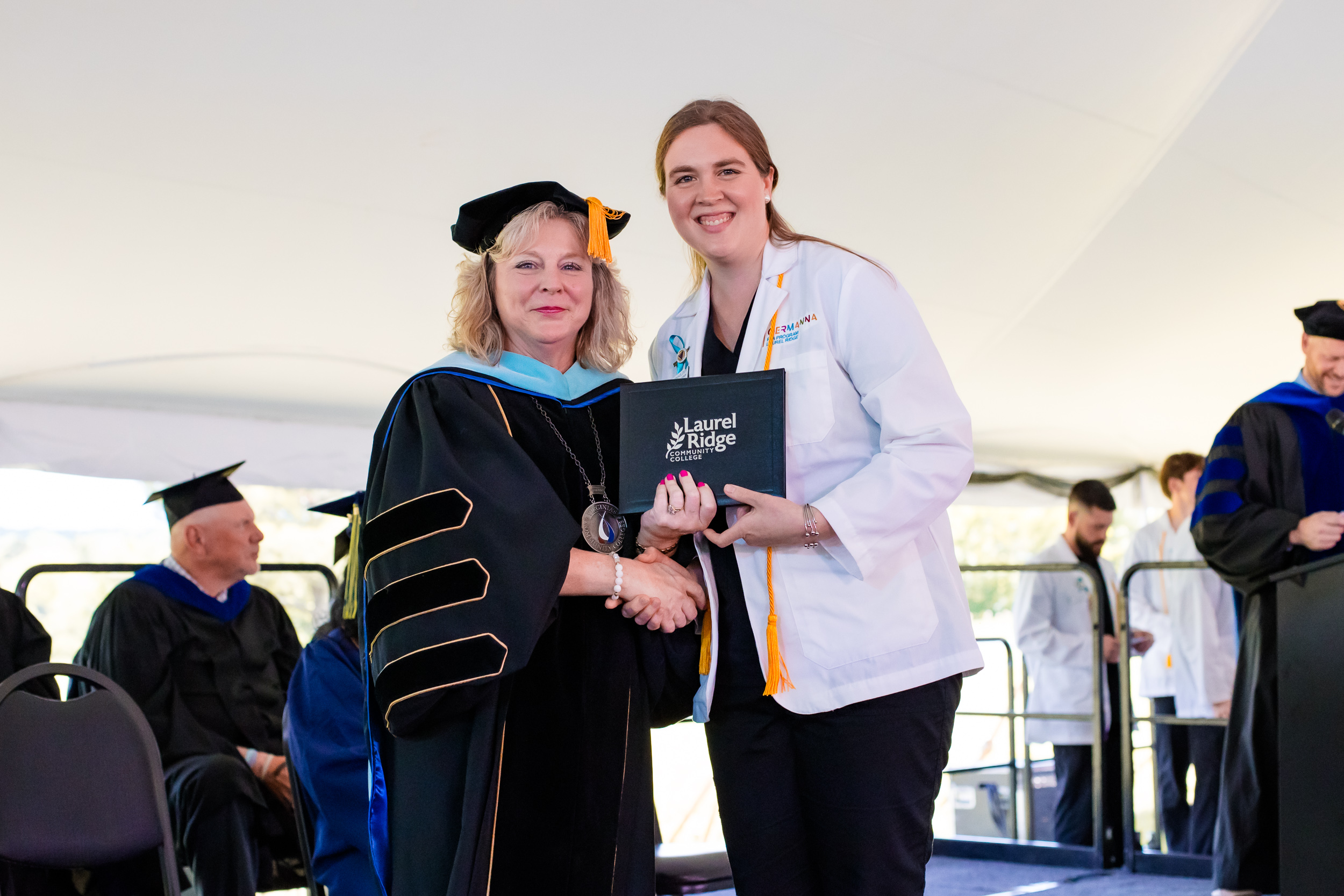 Julie holding her diploma and standing next to President Blosser on stage at commencement