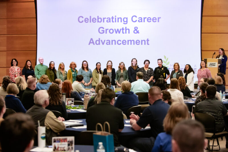 Group of Laurel Ridge Community College employees standing on a stage during a professional recognition event, with a large audience seated at tables and a projected screen reading “Celebrating Career Growth & Advancement” behind them