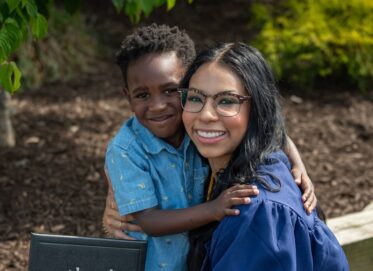 a photograph of a graduate hugging her child while holding a diploma cover