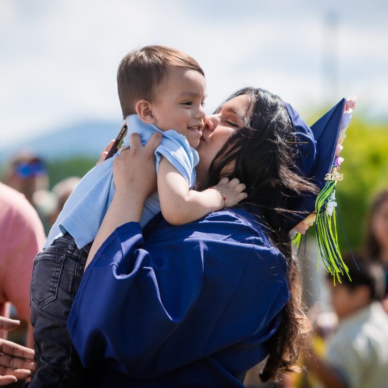 Graduate holding a small baby and giving it a kiss on the cheek