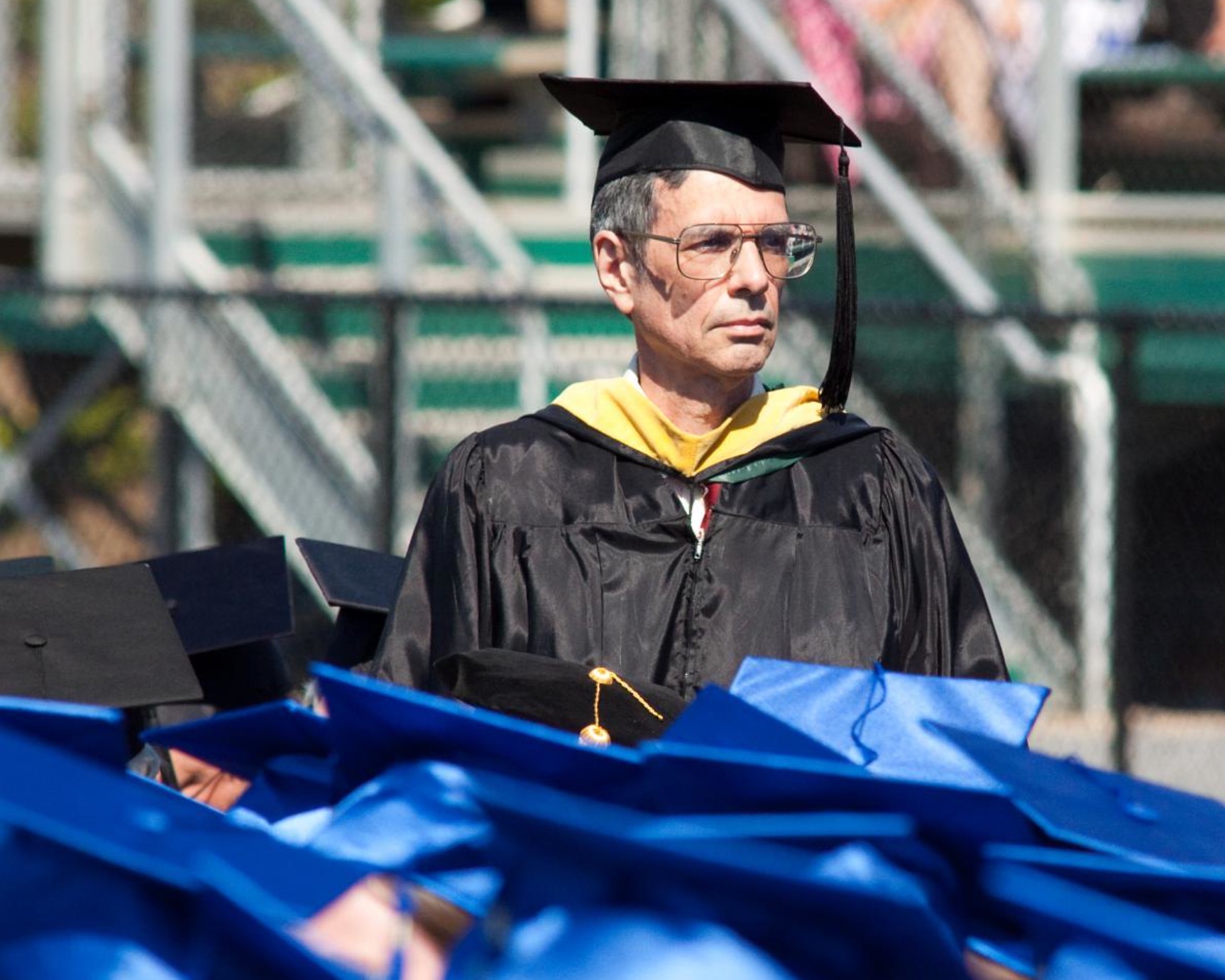 A photograph of a man in a black commencement gown standing in front of a bunch of graduates