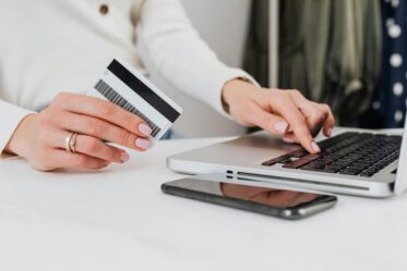 a photo of a woman's hands holding a credit card while typing on a computer