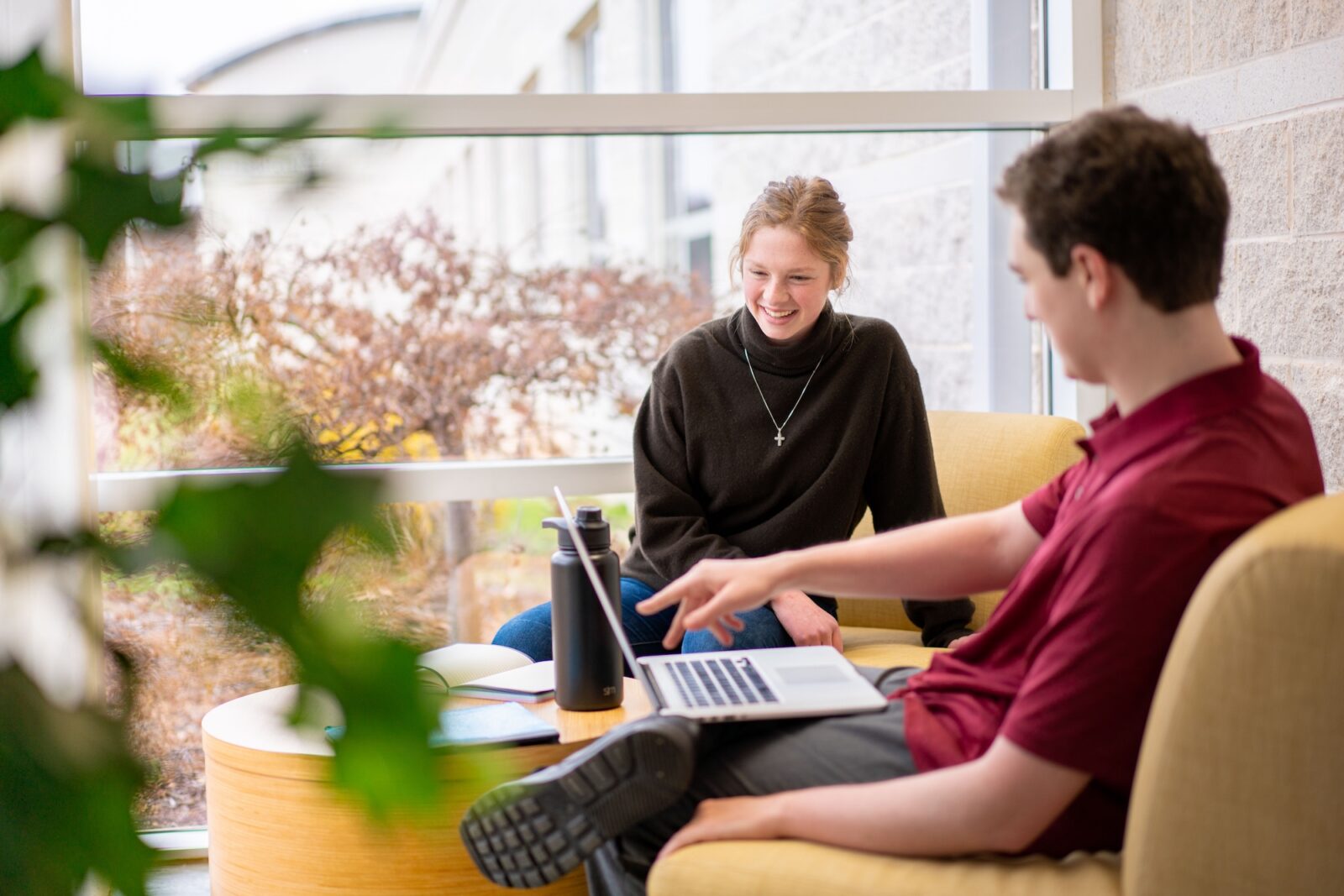 two students smile and look at a laptop in the lounge area of Wolk Hall