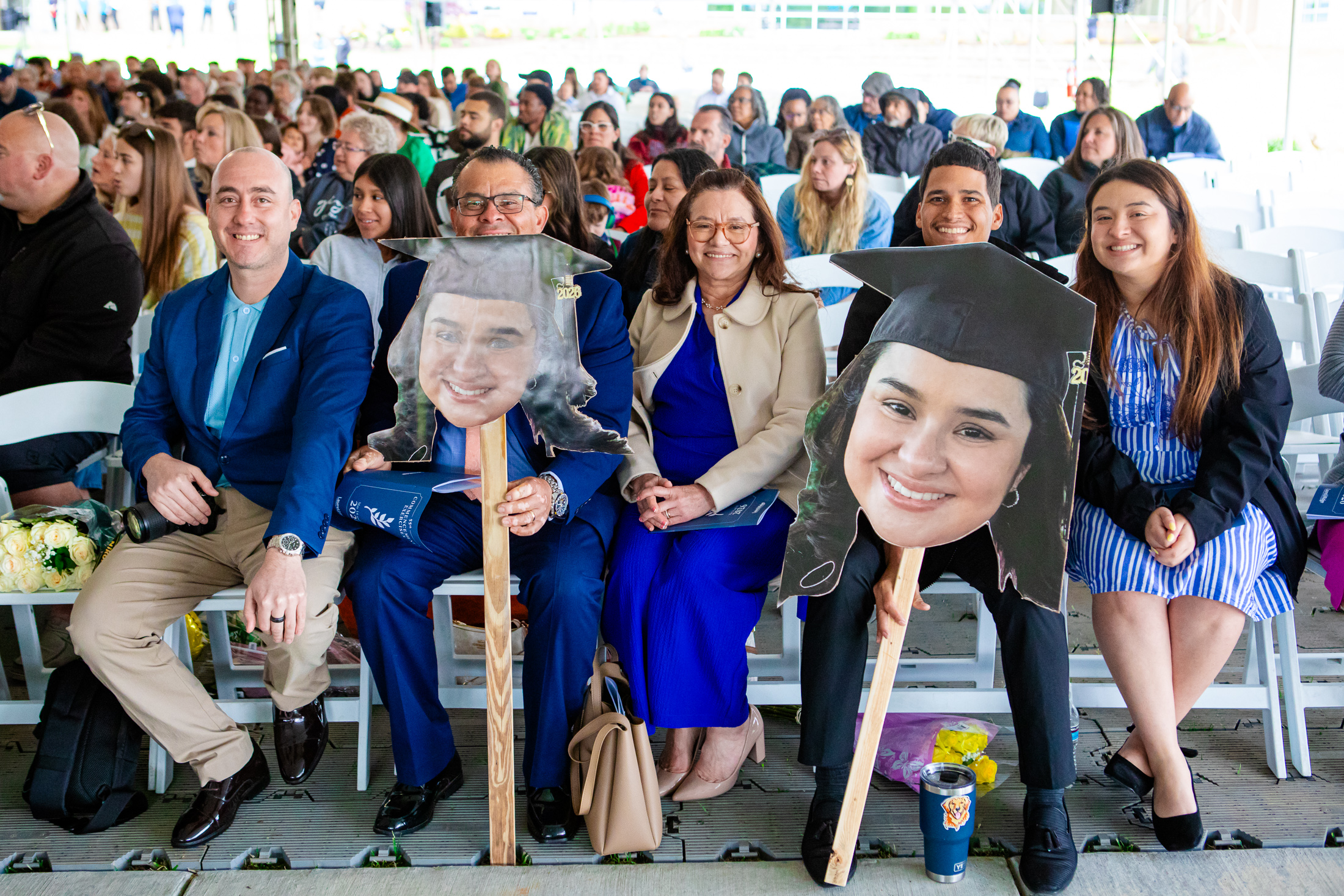Family members smile and hold large cutout photos of graduates wearing mortarboard caps while seated in the audience at the Laurel Ridge Community College commencement ceremony.