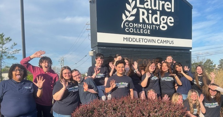 FEA students smiling and waving in front of the Laurel Ridge Community College campus sign.