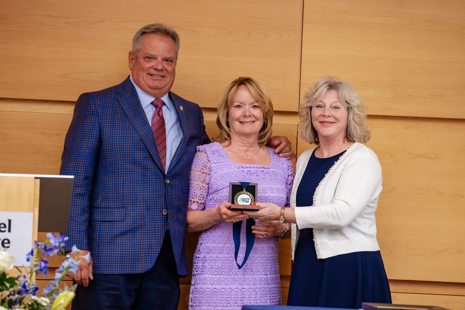 Bill and Sandy Stonebreaker Long pose with a Laurel Ridge Community College Medallion of Recognition at the 2026 ceremony. Sandy holds the medallion in its presentation box while flanked by Bill on the left and another woman on the right, all smiling for the camera.
