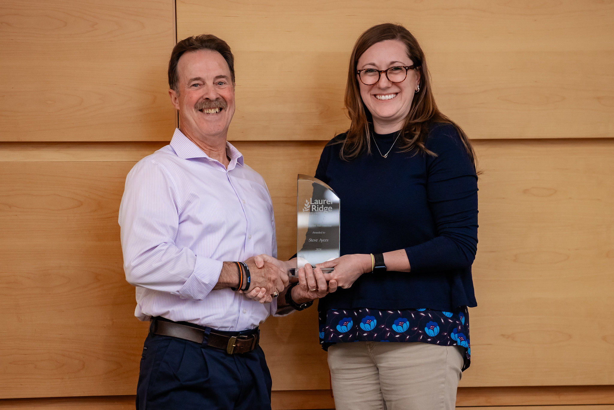 Steve Ayers and Whitney Miller smile while shaking hands and holding a Laurel Ridge Community College award presented to Steve Ayers.