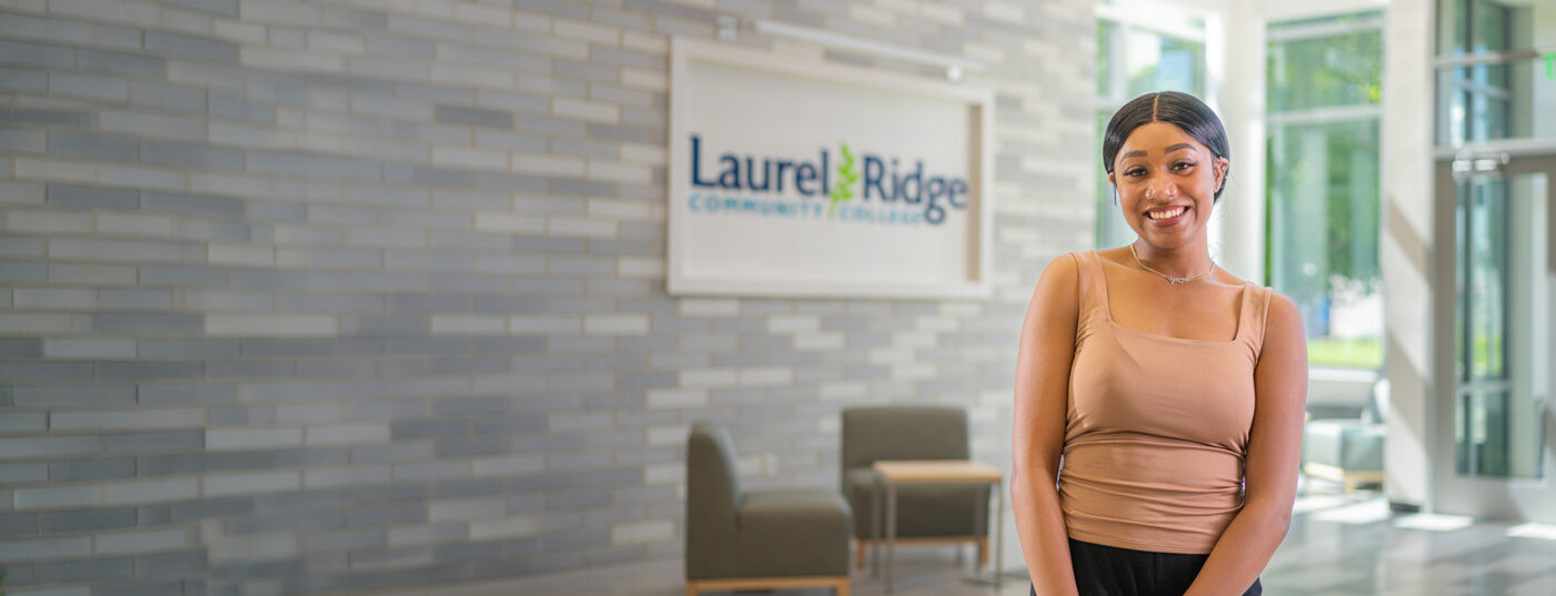 a smiling student stands in front of a laurel ridge community college sign