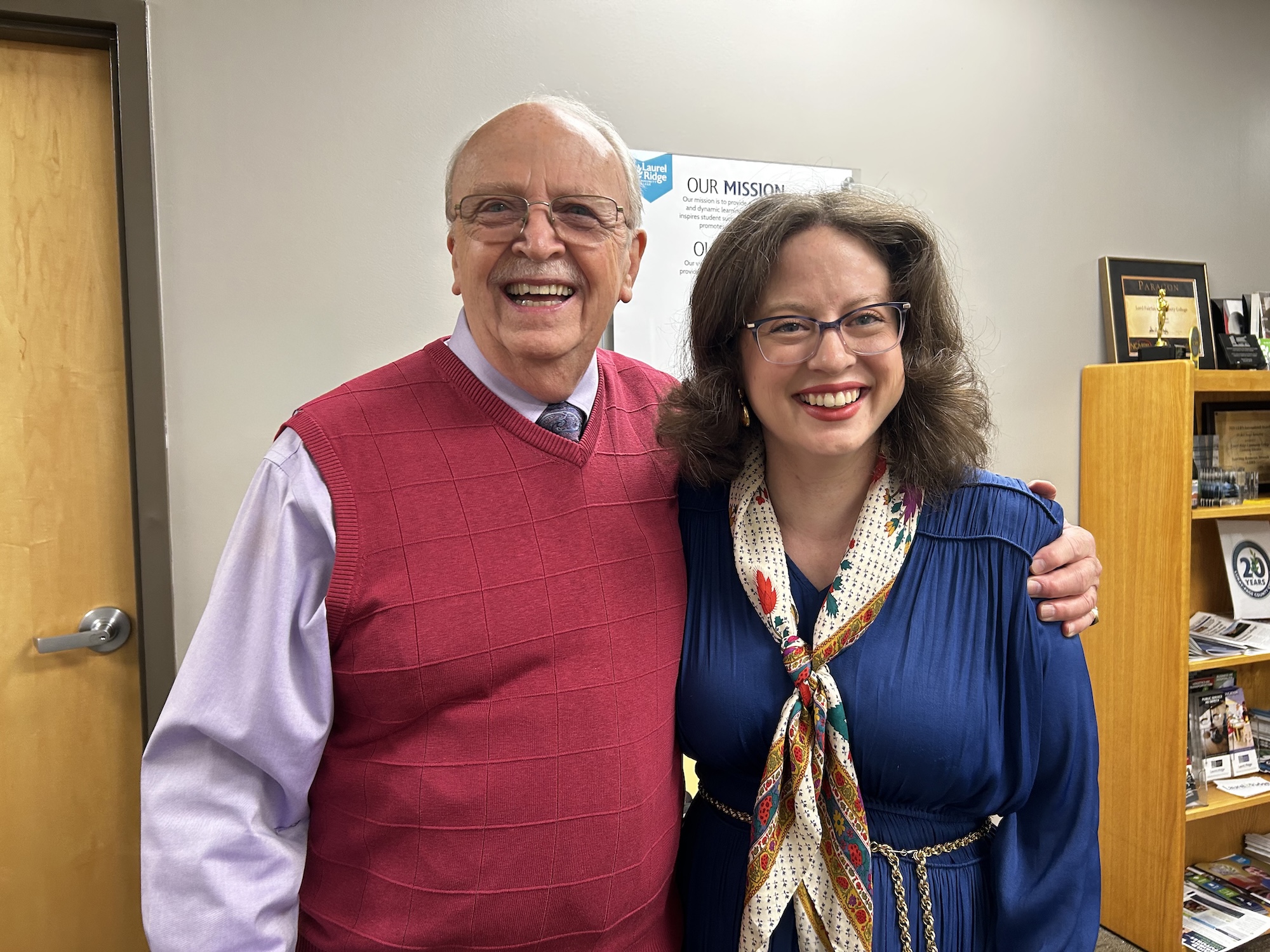 Brent Kendrick and Anna Groves smile together in an office, with a Laurel Ridge Community College mission statement poster and an award plaque visible on a shelf in the background.