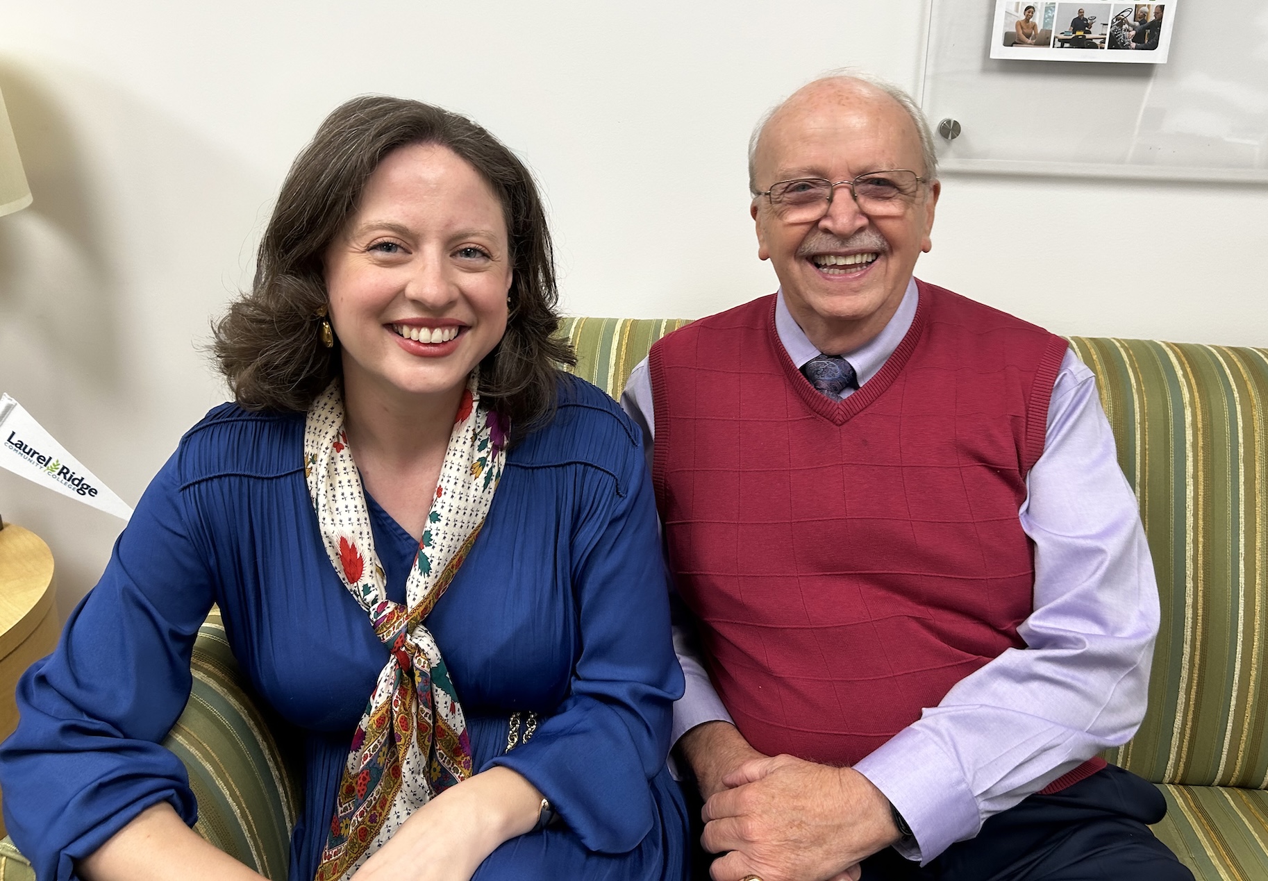 Anna Groves and Brent Kendrick smiling and sitting together on a striped couch, with a Laurel Ridge Community College pennant flag nearby