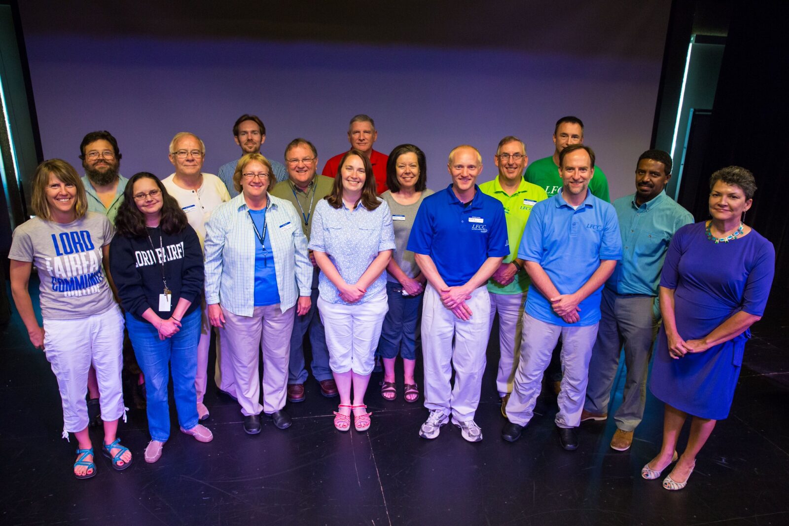 Group of faculty and staff standing together on a stage in a group photo.