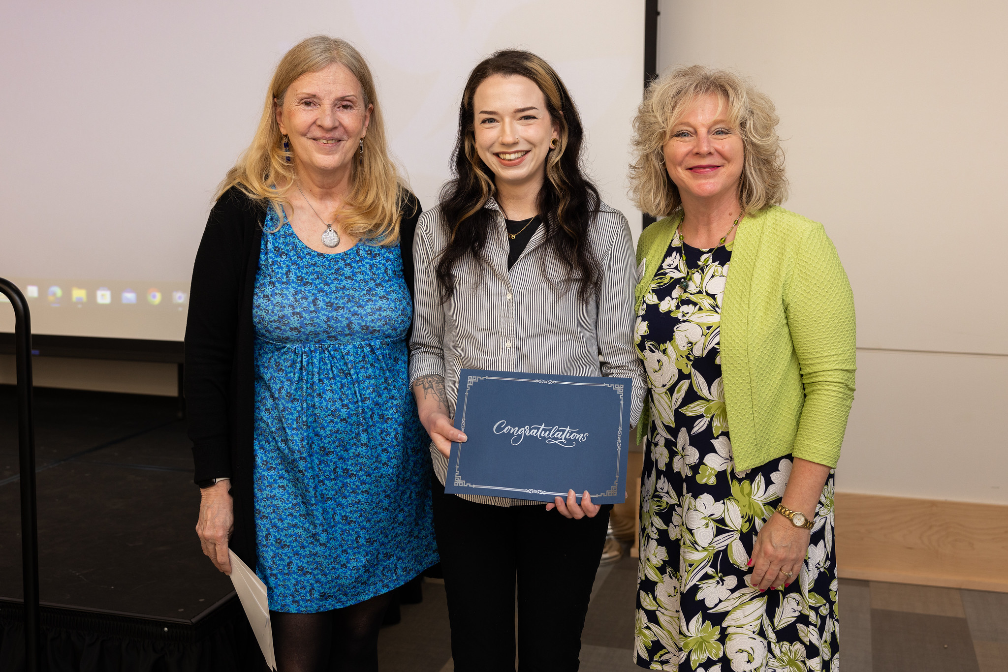 Three people posing with a certificate during an awards or recognition ceremony.