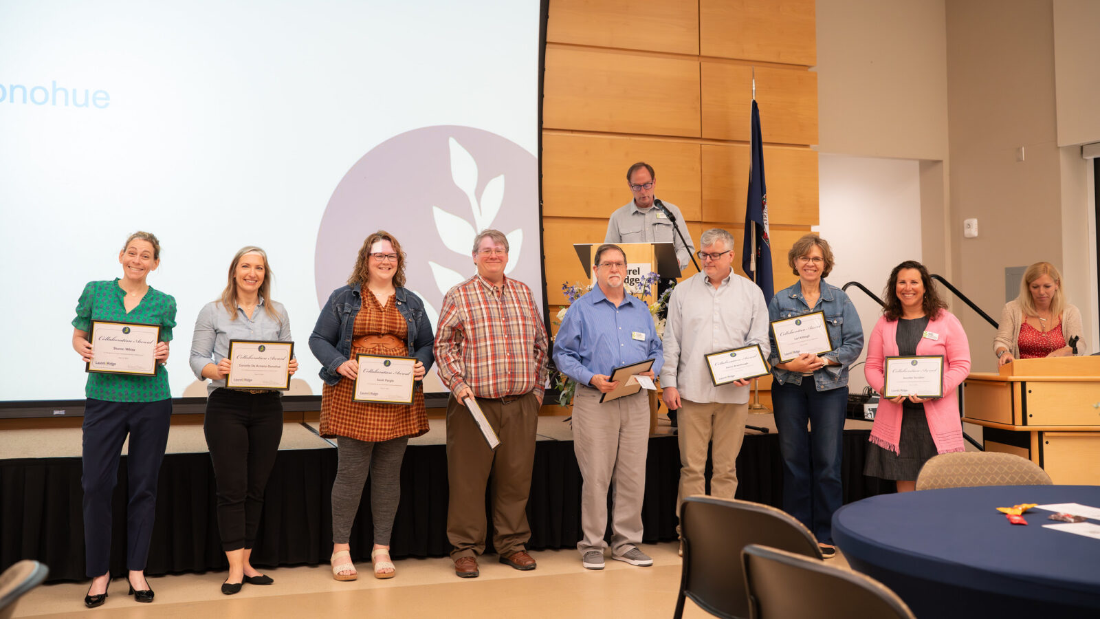 Nine people stand in a line on a stage at a Laurel Ridge Community College event, each of the eight in front holding a framed "Collaboration Award" certificate.