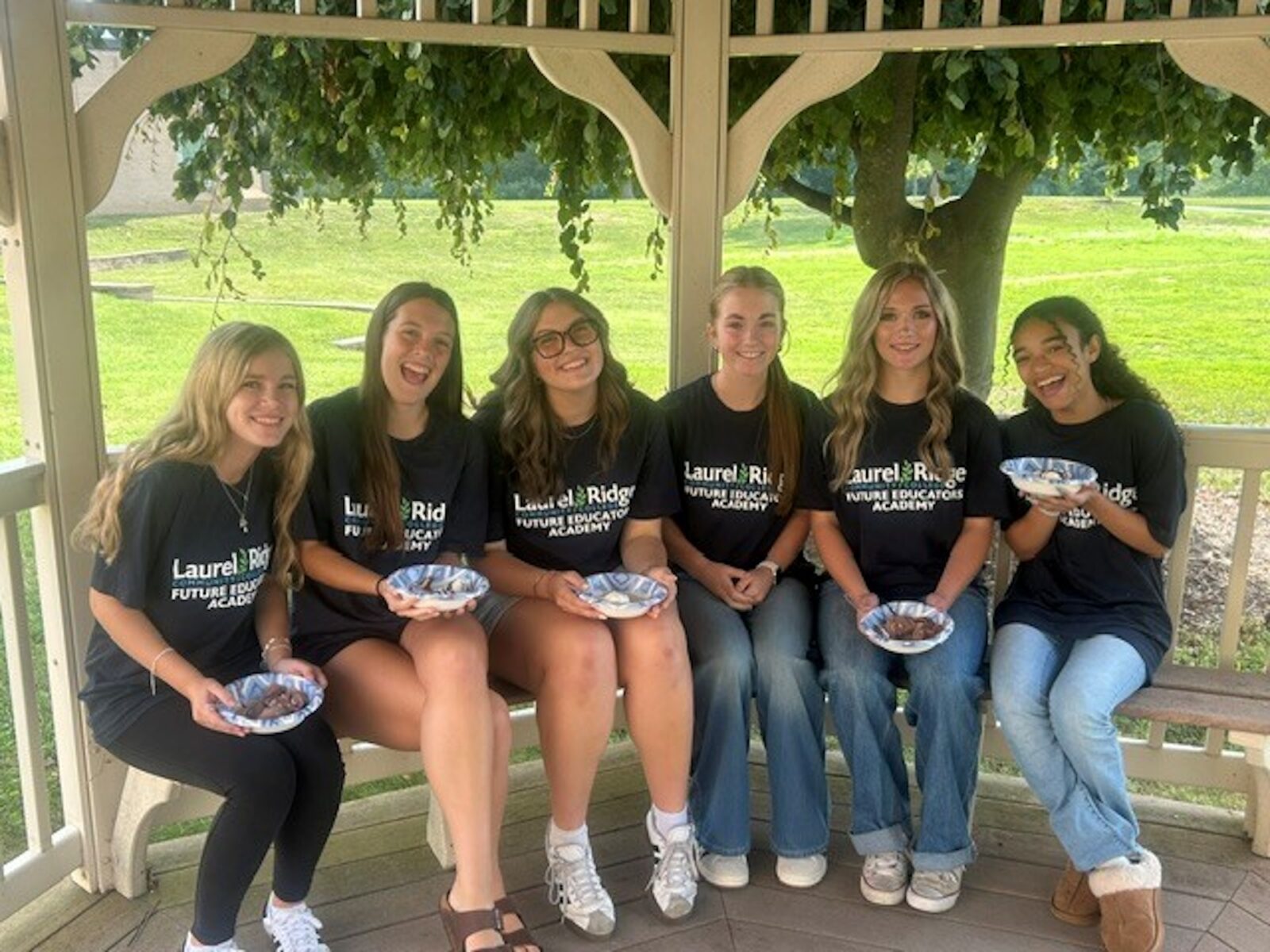 Future Educators Academy students in matching navy T-shirts sitting on a bench in a gazebo holding bowls of ice cream