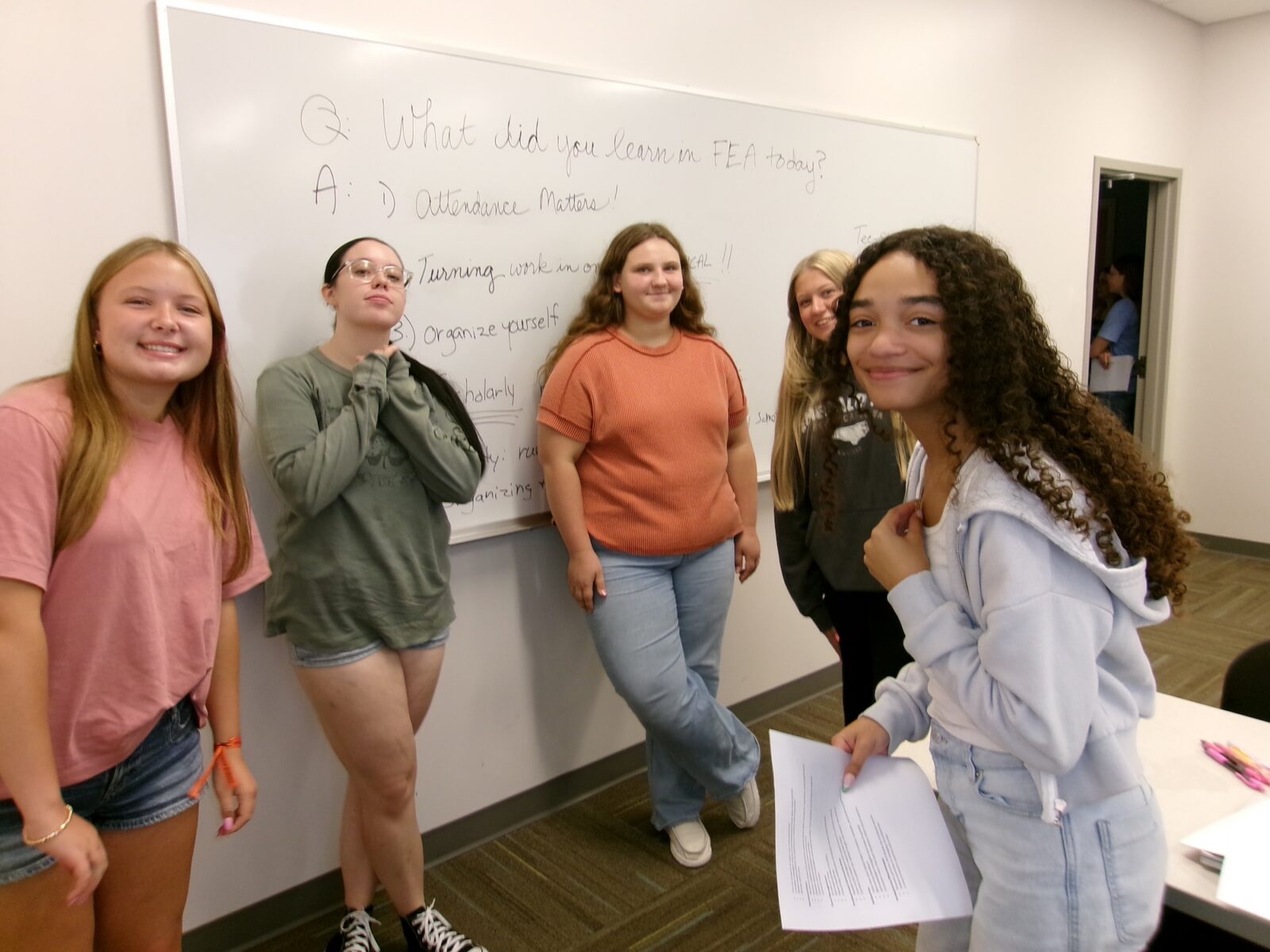 Students smiling in a classroom beside a whiteboard listing lessons learned in the Future Educators Academy