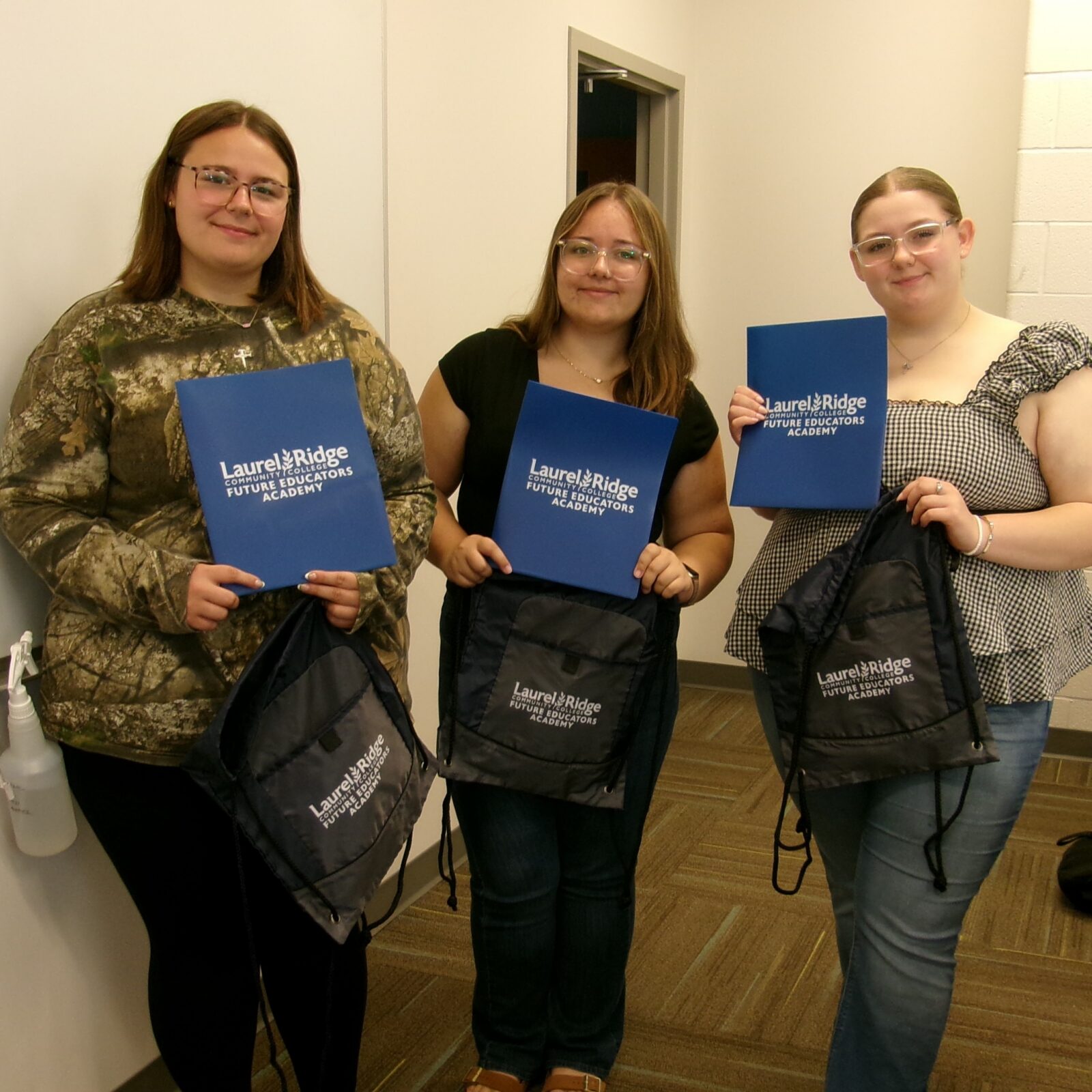 A group of 3 FEA seniors standing in their classroom with their blue FEA folders and cinch packs. 