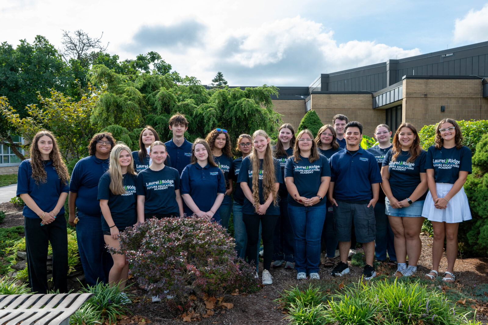 A group of FEA students standing in a garden setting in front of the campus.