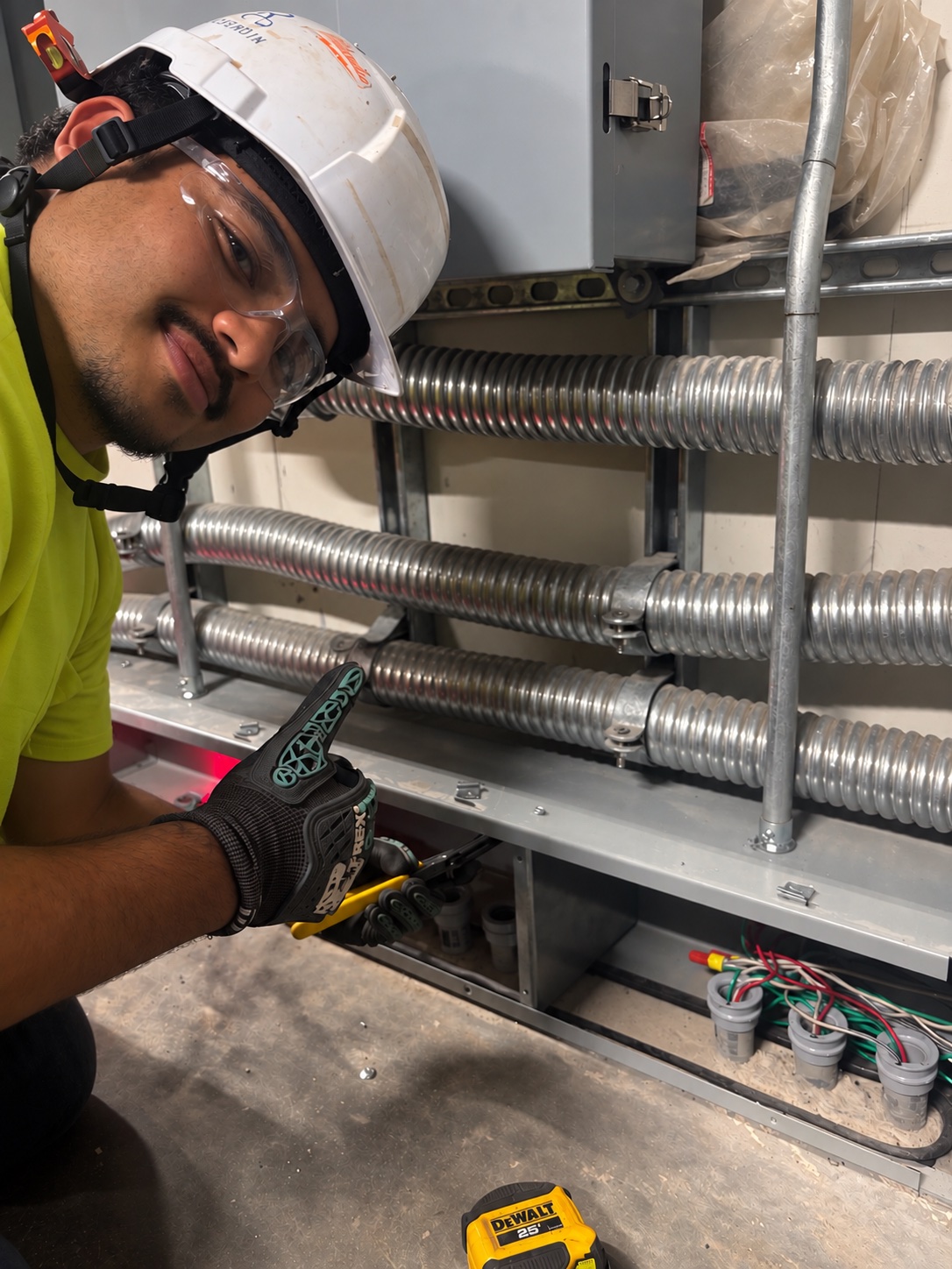 Oscar Burgoa, in a hard hat and safety glasses, points to a tool while working on electrical conduit.
